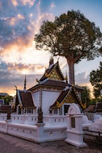A scenic view of Wat Chiang Man Temple with vibrant clouds and a tree at sunset in Chiang Mai, Thailand.