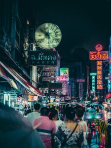 Bustling night market street illuminated by vibrant neon signs and crowds of people.